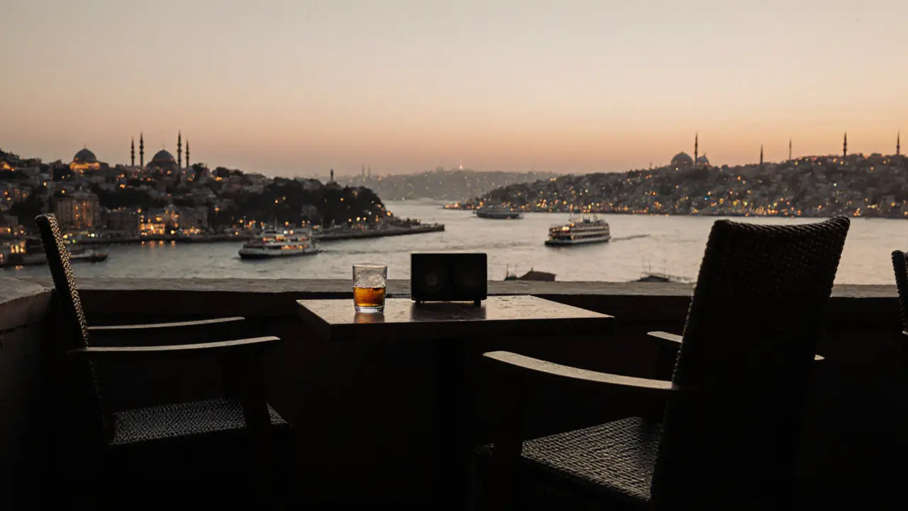 Rooftop view of Istanbul at dawn with empty chairs, a glass of rakı, and the Bosphorus glowing in the early morning light.